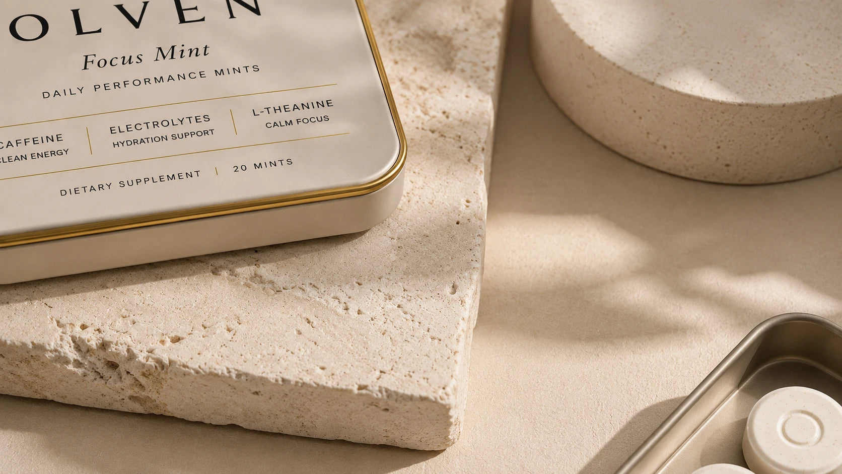 The Olven Focus Mint tin resting on travertine stone beside an open tin of mints, in warm afternoon light