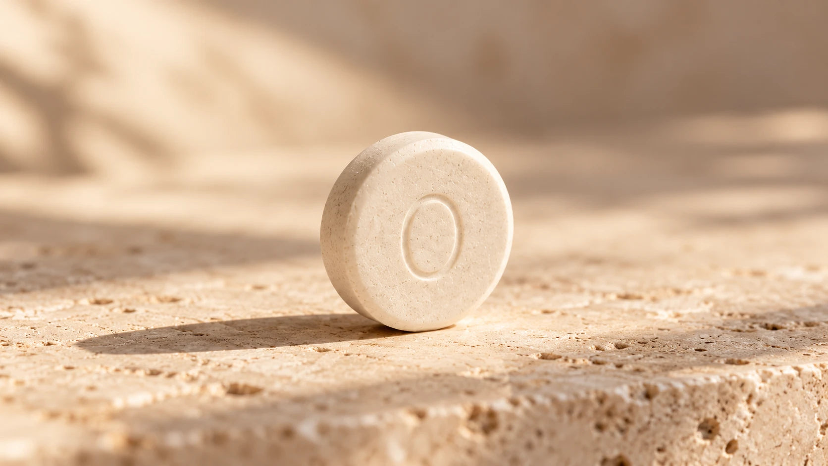 A single Olven mint with its embossed O, standing on travertine stone in warm light